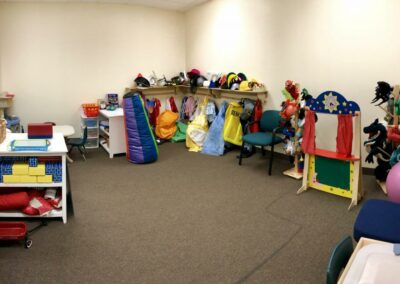 picture of play therapy room including dollhouse, puppets, costumes, blocks, chair ball, small table and chairs