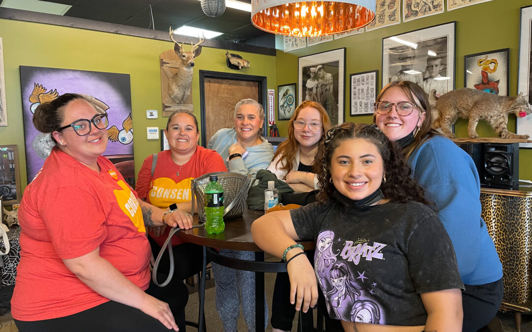 Group of six individuals standing around a table and smiling at Glory Bound Tattoo.