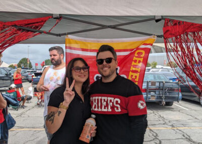 Two individuals at MOCSA's Chiefs tailgate party standing in front of Chiefs flag and smiling at the camera.