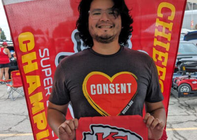 Chiko at MOCSA's Chiefs tailgate party wearing MOCSA CONSENT t-shirt and holding Chiefs Super Bowl flag