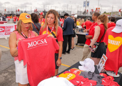 Two individuals looking at MOCSA t-shirts at Chiefs Charity Game tailgate suite.