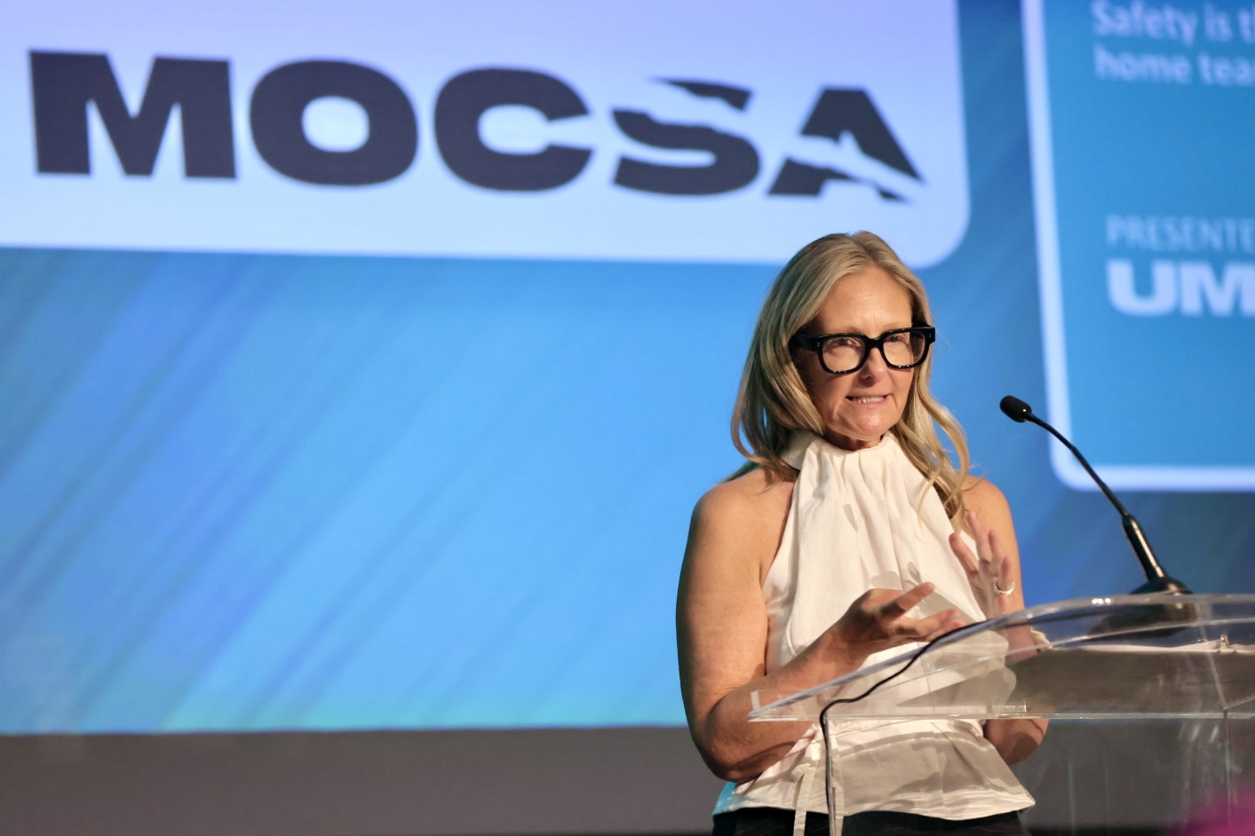 Eva Orner stands behind acrylic podium on stage