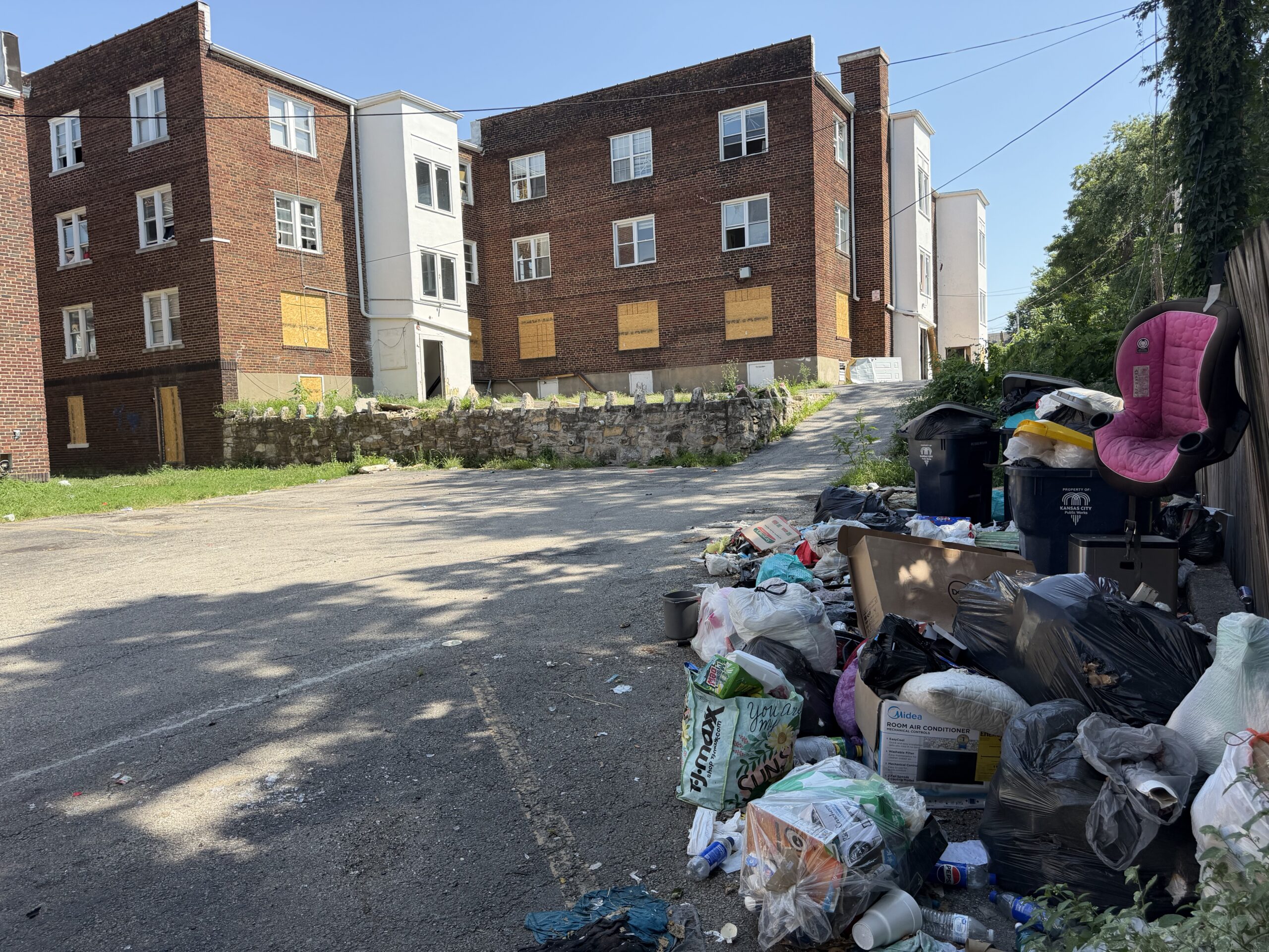 North Lawn Apartments exterior Exterior of North Lawn apartments with first floor windows boarded up and large piles of trash alongside a fence